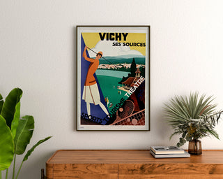 Vintage travel poster – Vichy, springs and tourism, framed above a wooden dresser between plants.