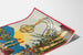 Vintage wine poster – Au bon vin d’Alsace – Hansi, shown on a curled sheet, perspective view.
