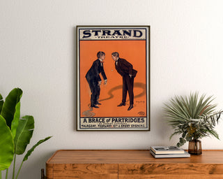 Vintage poster A Brace of Partridges, Strand Theatre, framed above a wooden dresser, flanked by plants.