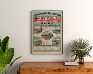 Vintage Auvergne poster, PLM excursions, framed above a wooden dresser, between plants.