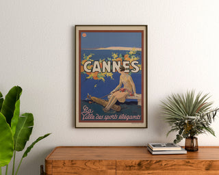 Vintage Cannes poster, Les Sports Élégants, framed above a wooden dresser between plants.
