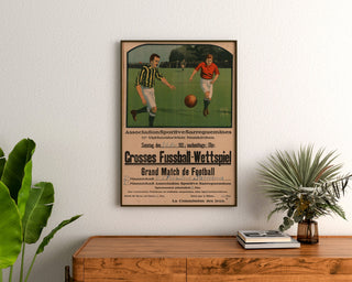 Vintage Sarreguemines poster, football match, framed above a wooden dresser, between plants.