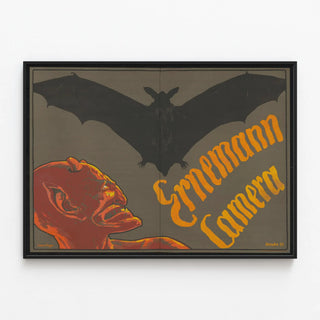 Vintage poster of Ernemann camera with demon and bat — framed artwork on a wall